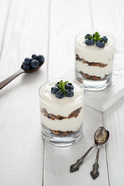 Dessert met kwark verse bosbessen en muesli in een glas op een witte houten achtergrond