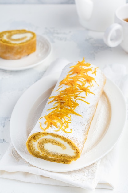 Dessert pumpkin roll with butter cream and orange server for the festive table on light gray table. Selective focus.