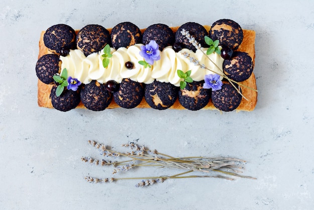 Dessert saint onore. berry pie. puff pastry tart with\
profiteroles, butter cream, black currant jam with fresh mint,\
lavender flowers and berries. gourmet french dessert on gray\
wall.