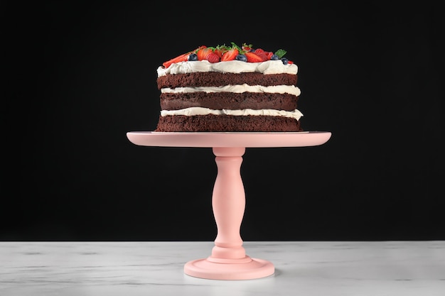 Photo dessert stand with delicious chocolate cake on table against black