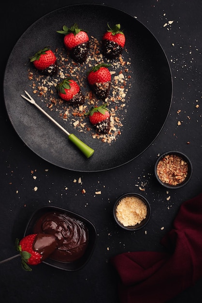 Dessert con fragole ricoperte di cioccolato su piatto nero su sfondo nero vista dall'alto