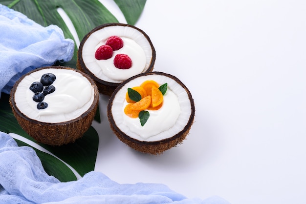 Dessert with cream and berries in coconut on white background with leaf and blue towel, smoothie bowls concept