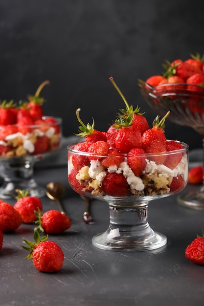 Dessert with strawberries, cottage cheese and biscuit in glass goblets against a dark surface, vertical photo