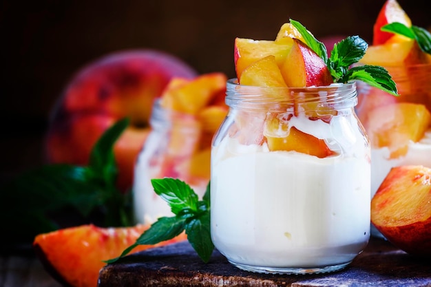 Dessert with sweet peaches cottage cheese and whipped cream served in glass jars vintage wooden background selective focus