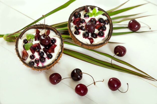 Dessert with whipped cream and cherries and currants in coconut cups on palm leaves