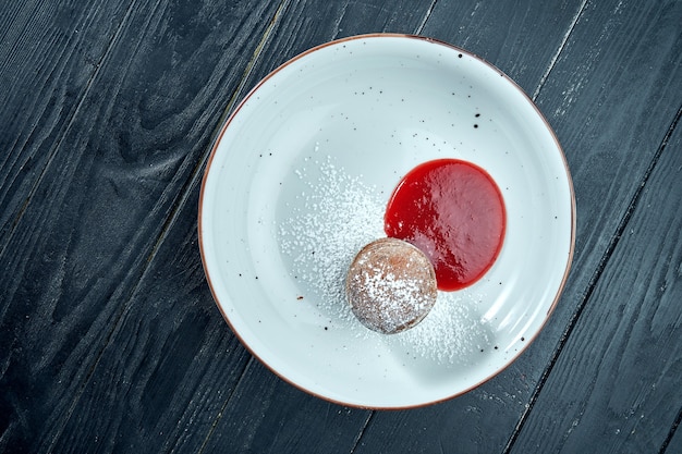 Dessertchocoladefondant met bessensaus en poedersuiker in een witte plaat op houten tafel