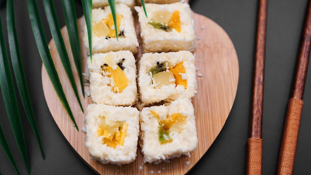 Dessertsushi. zoete kiwi, ananassushibroodjes. sushi op een houten dienblad op een zwarte achtergrond met een tropisch blad