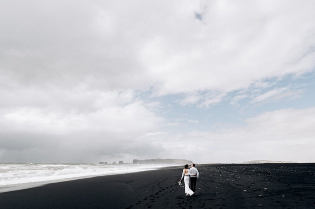 목적지 아이슬란드 결혼식 웨딩 커플이 빅 모래 해변의 검은 해변을 따라 걷고 있습니다.