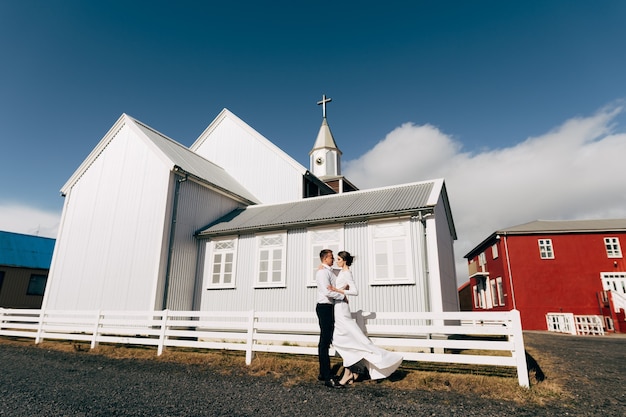 木製の黒い教会の近くの目的地のアイスランドの結婚式の結婚式のカップル新郎は花嫁を白く抱きしめます