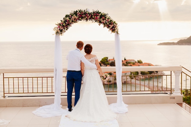 Destination wedding couple at sunset with wedding arch and sea background