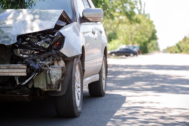 Photo destroyed car in car crash traffic accident on city road with copy space on city road. smashed broken front auto headlight, dented hood without bumper in car accident. auto life and health insurance.