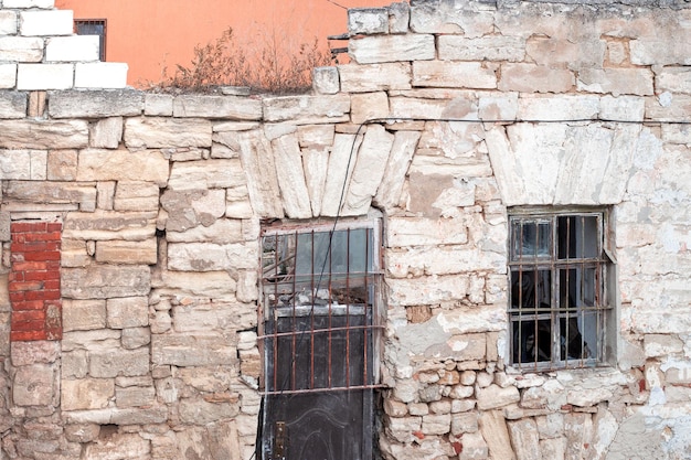 Destroyed stone wall of an old house with a door and a window.