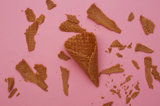 Destroyed waffle cone on pastel pink background.