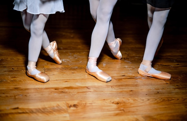 Foto dettaglio dei piedi dei ballerini di tre ragazze in piedi in posizione speciale sul pavimento di legno gambe delle ballerine in punta primo piano