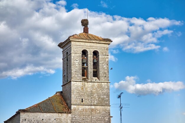 Detail of the bell tower of a rural church with stork nests on its roof and a nice blue cloudy sky behind