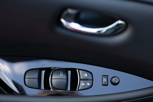 Detail on buttons controlling the windows in a car. car\
interior details of door handle with windows controls and electric\
mirrors adjustments. window and mirror control panel on driver\'s\
door