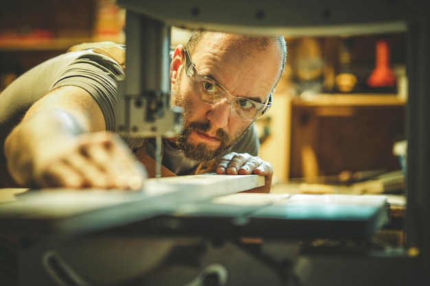 Dettaglio di un falegname al lavoro tagliando una tavola con una sega a nastro nel suo laboratorio