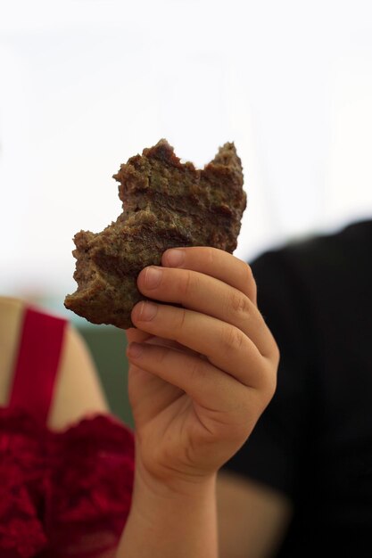 Detail of a caucasian little child girl hands eating a hamburger in the cafe Fast food over blurred background Unhealthy food Toddler baby girl enjoying a burger child's hands holding bitten meat