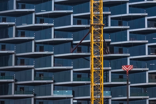 Detail of a construction crane against the background of the glass facade of a beautiful skyscraper