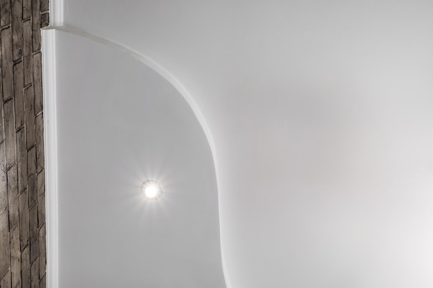 Particolare del soffitto ad angolo con intricate modanature a corona soffitto sospeso e costruzione in cartongesso in una stanza vuota in un appartamento o in una casa soffitto teso bianco e di forma complessa