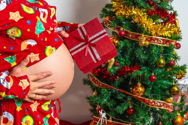 Detail of a couple hugging each other delivering christmas gifts next to the christmas tree family with pregnant woman