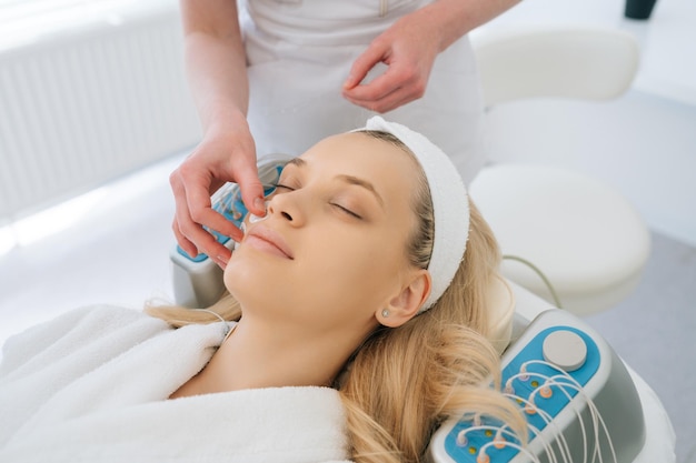 Detail cropped shot of unrecognizable beautician applying electrodes of myostimulator to woman face during bioresonance therapy in modern beauty clinic Concept of antiage rejuvenation skincare