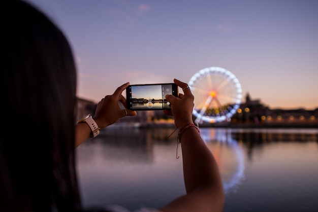 Foto dettaglio di una ragazza che fotografa una ruota panoramica con il cellulare