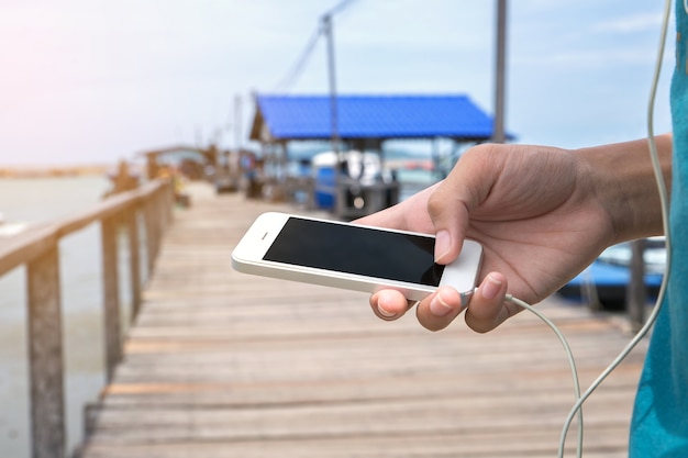Деталь рука смартфона при прослушивании музыки с наушниками на мосту