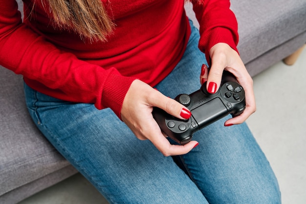 Detail of the hands and the controller of a young woman playing video game at home