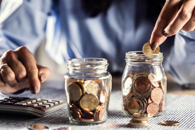 Detail of hands counting coins in two jars on a calculator