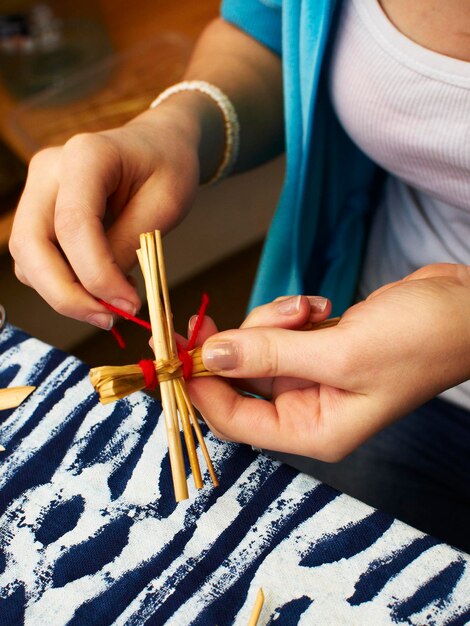 わらのクリスマスの飾りを作成する手のディテール。