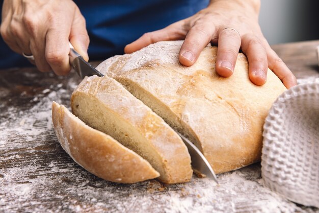 Detail of hands cutting a loaf of bread in slices