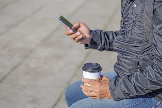 Detail of the hands of a Latin man holding a disposable cup with coffee and a mobile phone