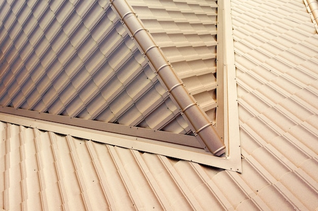 Detail of a house roof surface covered with brown metal tile sheets.