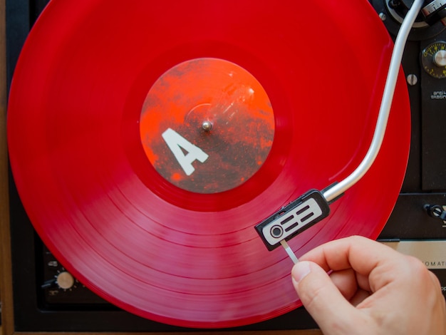 Detail of a male hand placing the needle on the track of a red vinyl record Vintage turntable