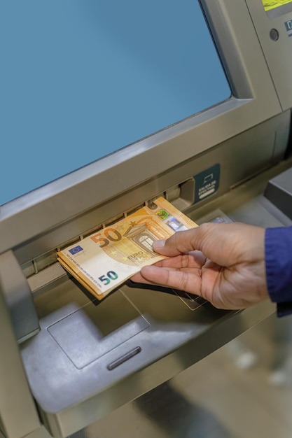 Foto dettaglio della mano di un uomo che tira fuori banconote in euro da un bancomat