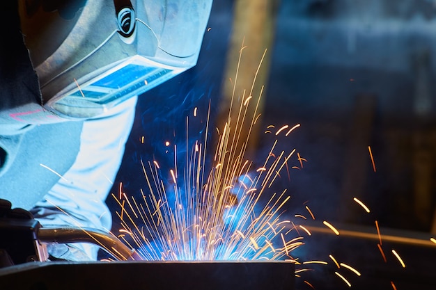 Detail of metal worker welding with welding mask sparks flying blue and orange