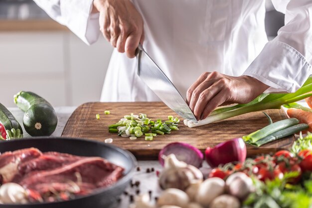 写真 生肉と野菜の材料を囲んだカッキングボードで春のニンジンを切っている人の詳細