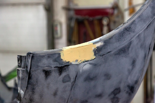 写真 鉄製の損傷した車のバンパーの詳細は、サンディングと塗装のために準備されたパテとグラウトを使用してワークショップで修復されます