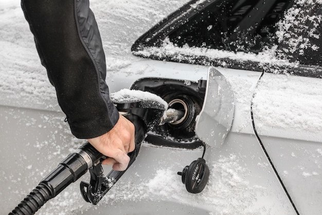 写真 燃料ノズルを持っている人間の手の詳細、冬に雪で覆われた車のガソリン タンクを充填