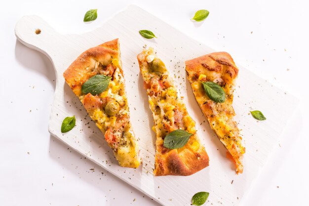 Detail op Drie stukken van Portugese pizza met basilicum bladeren op het witte bord