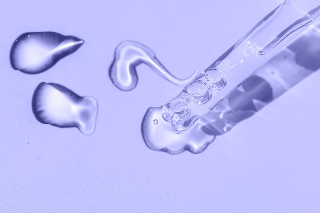 Detail of a pipette with pouring serum and droplet with shadow on a violet background