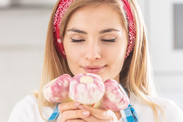 Detail of a pretty young girl smelling fresh garlic in her hands.