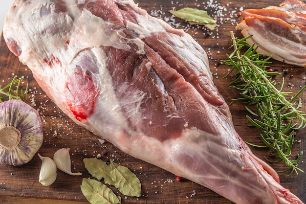 Detail of raw lamb chop on a wooden board with garlic, bay leaves, rosemary and bacon.