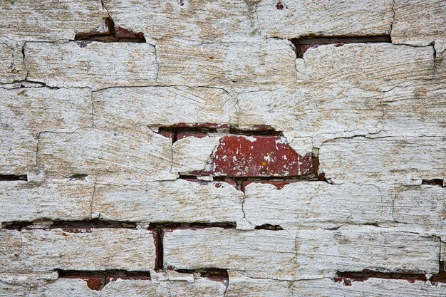 Деталь стены из красного кирпича, выкрашенная в белый цвет и распадающаяся с трещинами