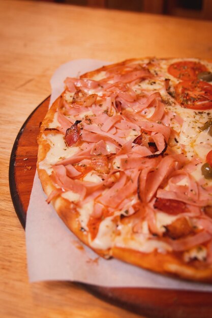 Detail shot of a pizza with ham on top of a wooden table