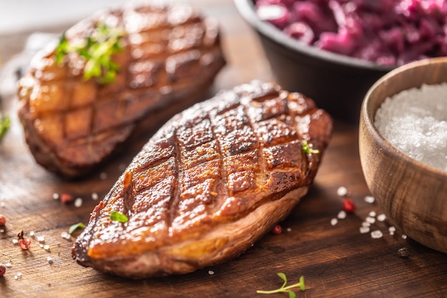 Detail of tasty roasted duck breasts and stewed red cabbage on a wooden cutting board.