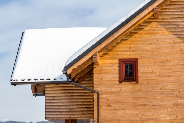急勾配の屋根、屋根裏部屋が晴れた冬の日に雪で覆われた木材材料の伝統的な木造の生態学的なコテージの詳細トップ。古い伝統と現代のプロの建築コンセプト。