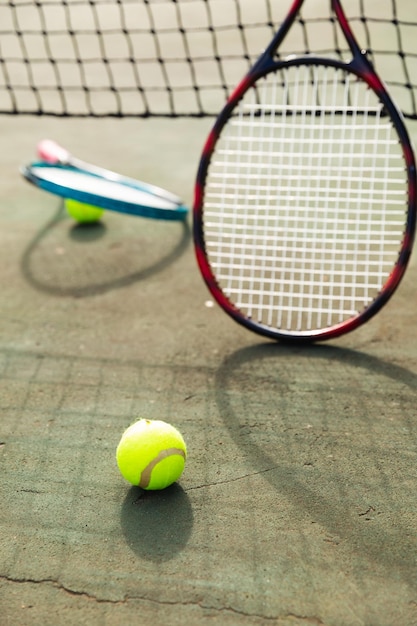 Detail of two tennis rackets and balls by the net at an outdoor tennis court, selective focus. Sport, healthy hobbies, competition, fitness and leisure time concept.