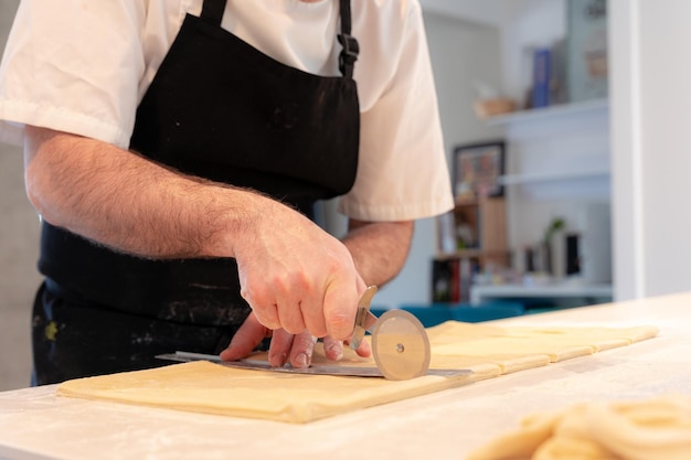 Detail van de handen van een man die croissants kookt die het bladerdeeg meet en thuis snijdt